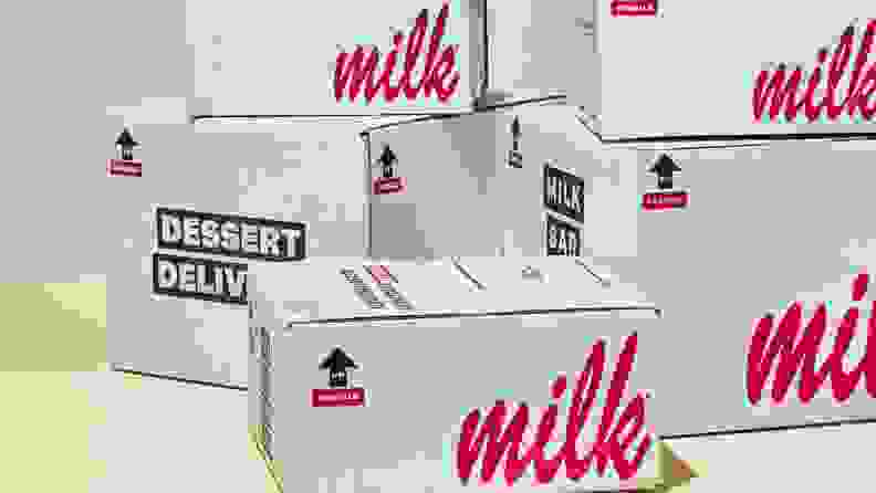 A stack of white cardboard boxes with pink cursive on the sides that read, "milk."