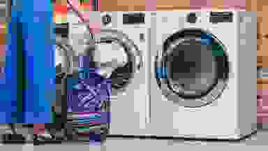 Woman loading a white towel into the white LG WM3700HWA front-loading washing machine, which is sitting next to a matching front-loading dryer.
