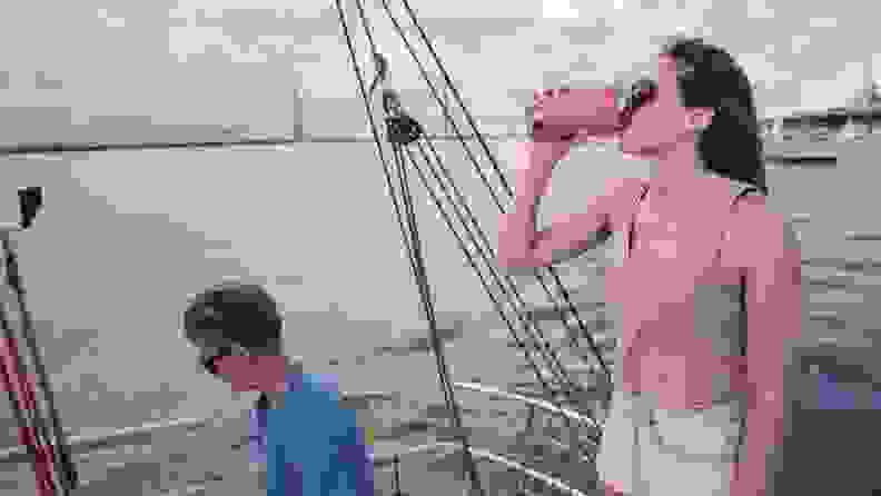 Two people on a boat, the woman is standing up and drinking from a reusable mug