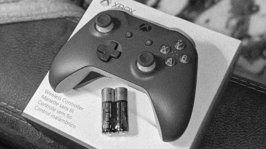 Close-up of an Xbox One wireless controller resting on its packaging. A pair of Duracell double-A batteries sit below it in plastic wrapping.