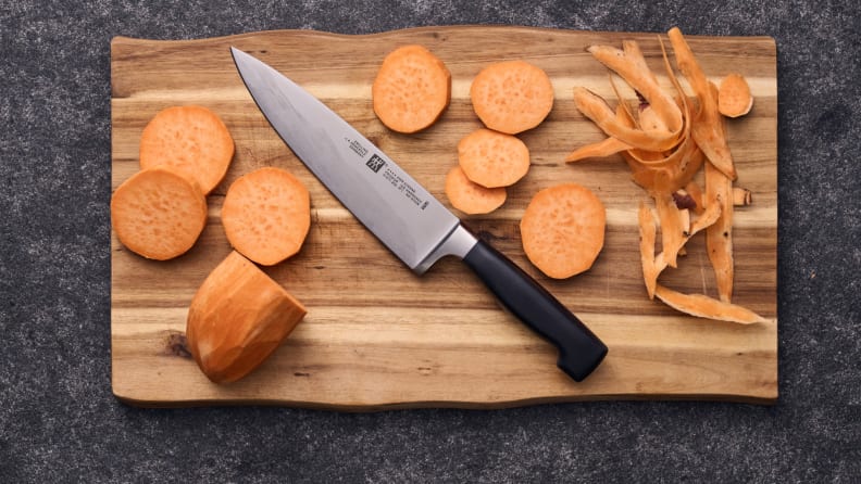 Black handled Zwilling chef knife on a cutting board with sliced sweet potatoes