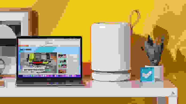 The Molekule air purifier sits on a desk next to a laptop displaying the Reviewed website and some contemporary desktop decorations, including a potted plant and the Reviewed logo.
