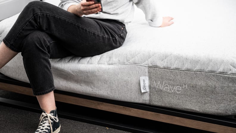 A person comfortably sitting down on the edge of a mattress