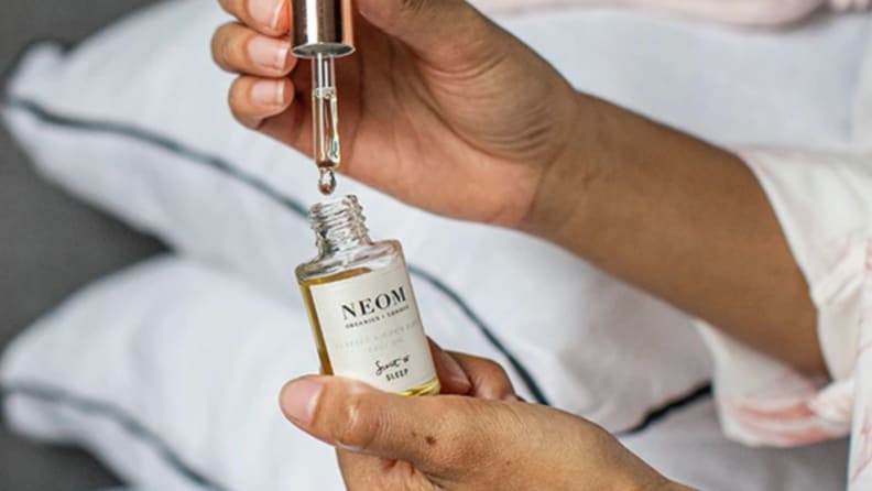 a woman fills a dropper with Neom Organics Sleep Face Oil
