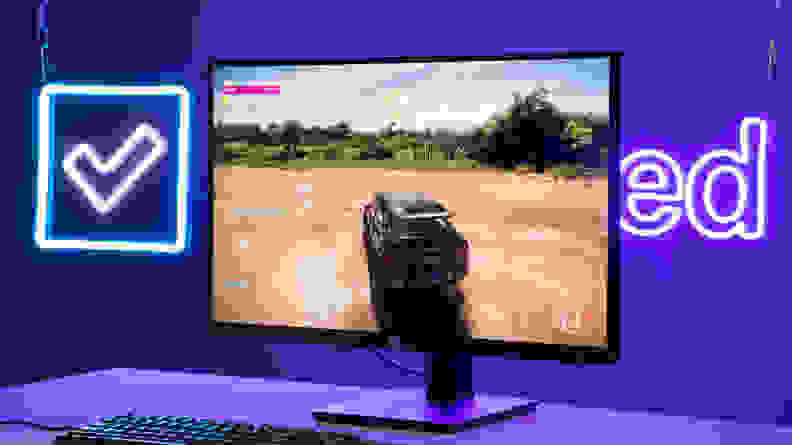 The monitor displaying a racing video game in front of the Reviewed.com neon sign.