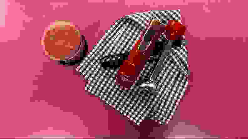 The Galanz Retro Immersion Hand Blender in the color red, laying on a black and white checkered towel, next to a glass of red juice.