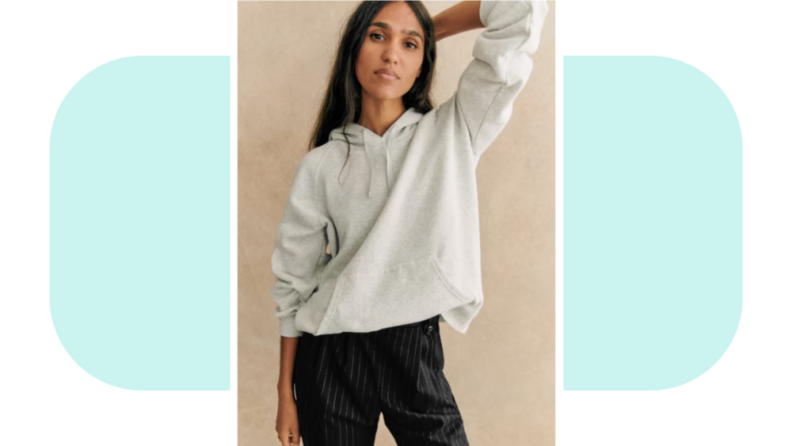 A model wearing a gray hoodie sweatshirt tucked into pinstripe pants.