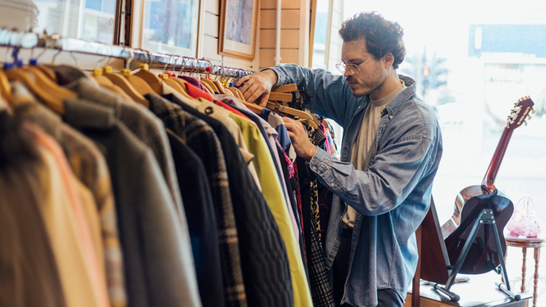 Person sifting through clothing rack inside of thrift store.