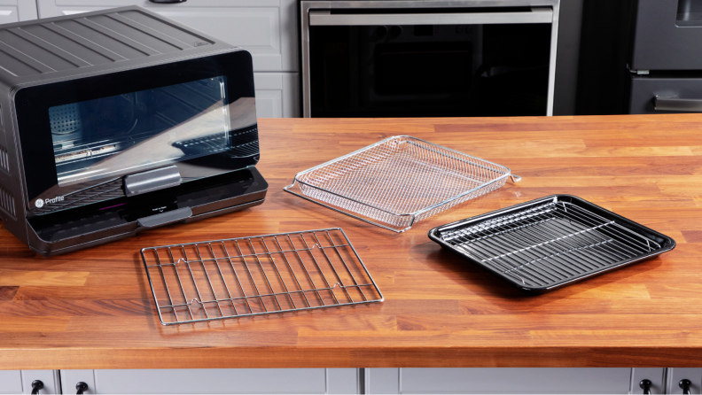 The GE Profile smart oven with its rack, baking pan, and air fry basket laid out on a wood counter.
