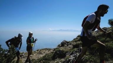 A group of three hiking together in the mountains, blue sky stretching out behind them