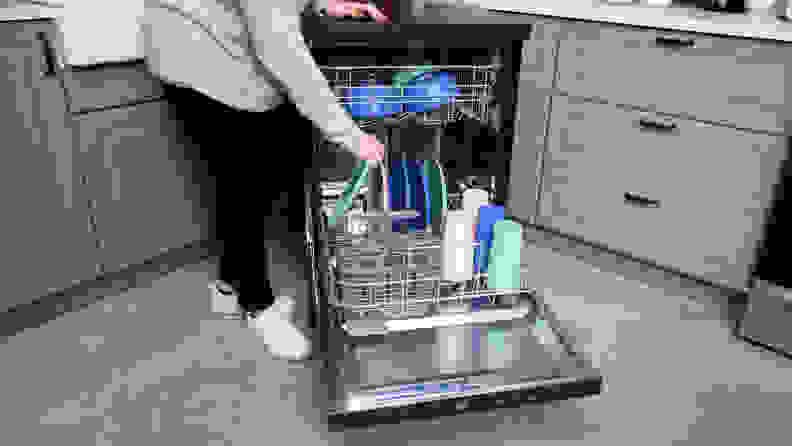 The GE GPT225SSLSS portable dishwasher,open and being filled with colorful pastel dishes.