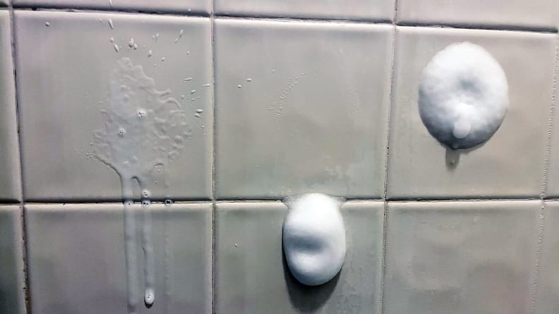 An image of the tilled side of a shower, showcasing three tiles in particular, all of which have been sprayed with a cleaner. The leftmost spray is very thin and runny, with barely any foaming action visible. The middle spray is a small dollop of foam, but in the time it took us to quickly spray and take the photo it had already run down about three inches, onto the next tile. The final spray is another circular mound of foam, only this time it's stuck to the center of the tile where we initially sprayed it.