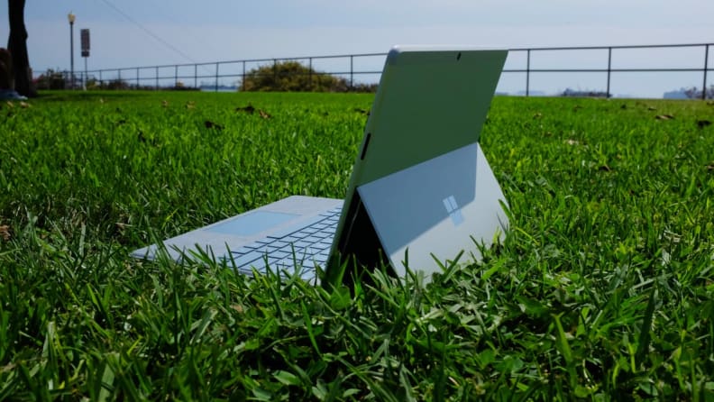 The Surface Pro X propped up by its kickstand on a field of grass.