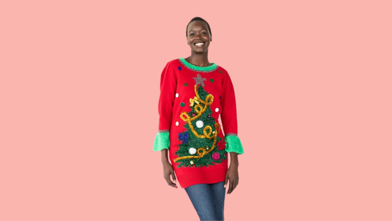 Woman wears a red ugly Christmas sweater dress with a Christmas tree on it.