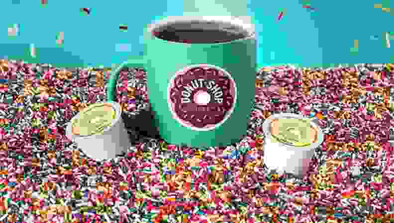 A bright teal coffee mug, surrounded by a sea of multicolored sprinkles.