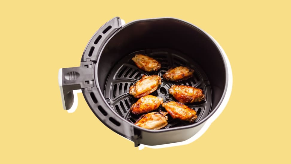 A batch of chicken wings in an air fryer basket, on a yellow background