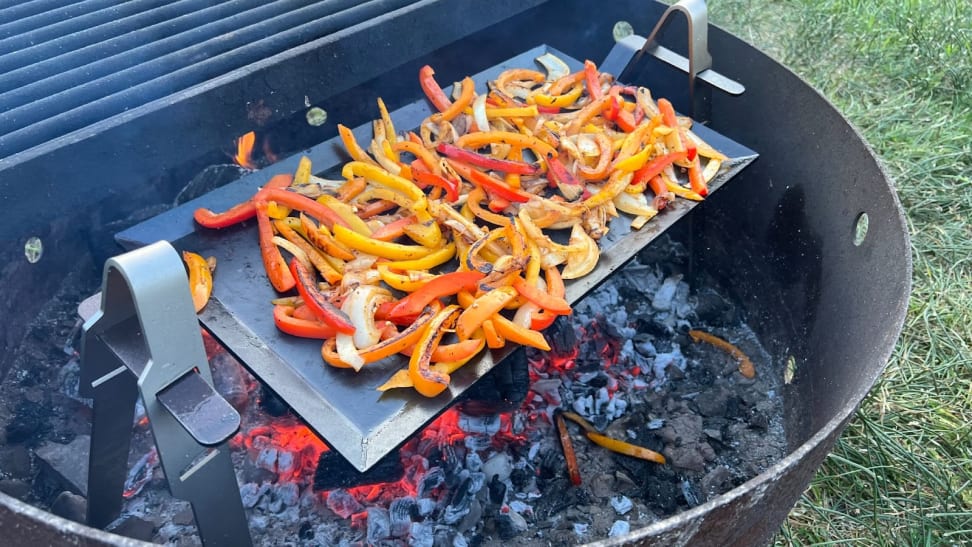 Red, yellow peppers and onions roasting outdoors on Made In Carbon Steel Griddle System on top of coals.
