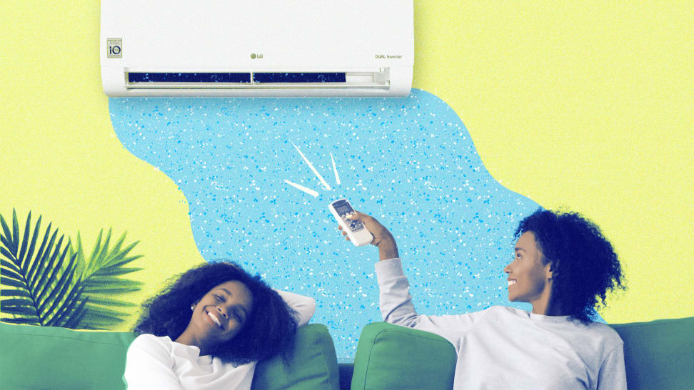 Two women sitting on a green couch, one woman is pointing a remote at an air conditioner mounted to a yellow wall.