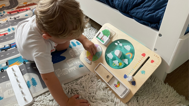 A toddler plays with a wooden weather chart.