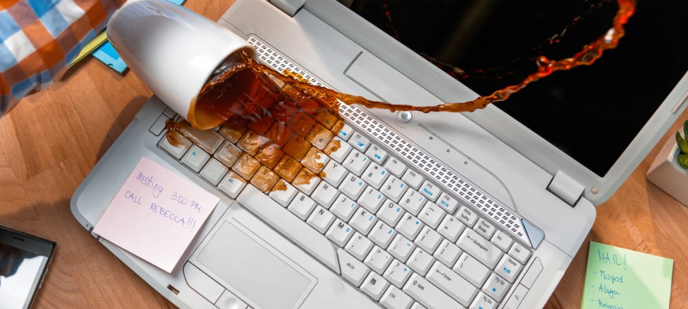 A mug of coffee spills over a laptop keyboard and splatters liquid all over the surface.