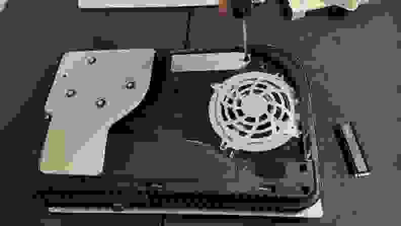 The Sony Playstation 5 uncovered with the cooling fan on display and a screwdriver untwisting open the expansion slot.
