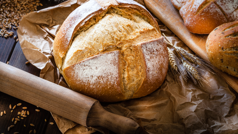 A loaf of homemade bread in an artfully composed close-up with a rolling pin beneath it.