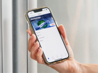 Person holding up smart phone to stainless steel refrigerator door with the Home Connect app on screen.