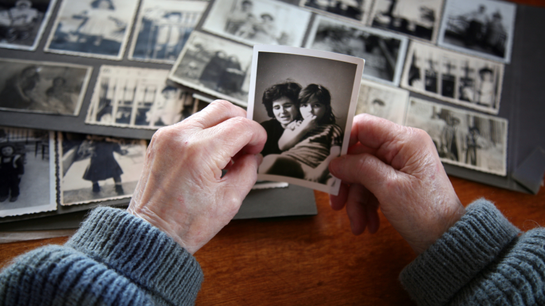 Hands holding photograph in front of photo album at table.