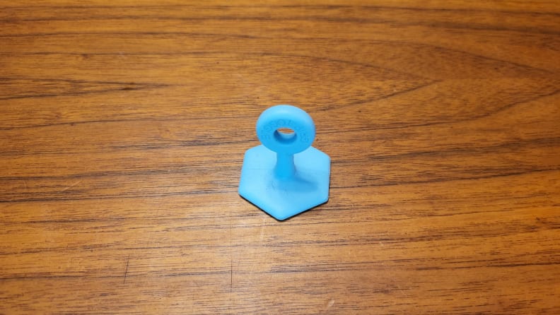 A blue Grip Toggle sits attached on a wooden surface. It has a loop at the top for pulling.