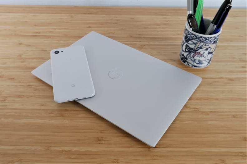 A closed laptop on top of a desk with a cell phone on top and a cup of pens behind it.