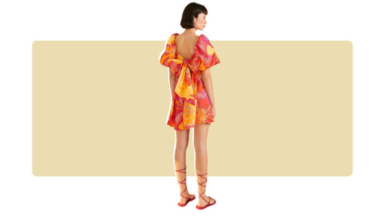 A mini dress with oversized red, pink, orange, and yellow floral print. There is a large bow tied along the back of the dress.