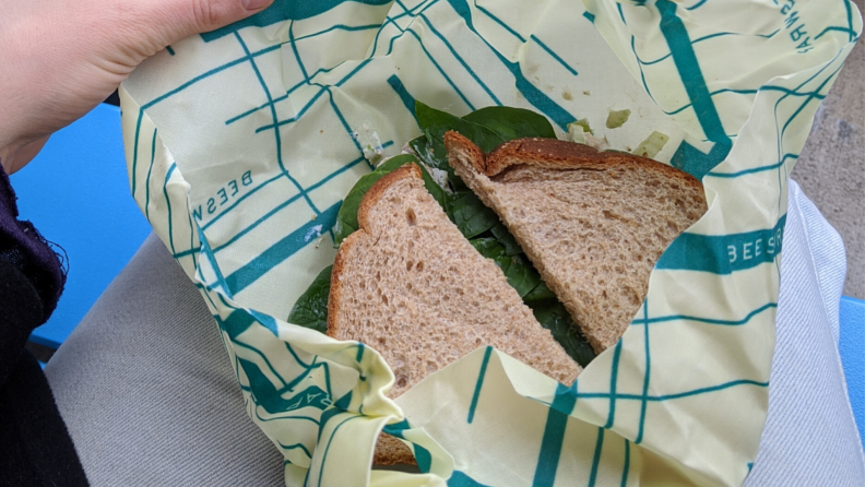 Person opening up Bee's Wrap on lap with sandwich inside