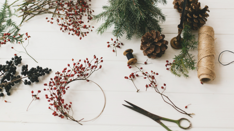 An overhead shot of pine needles, winterberries and other wreath supplies against a white background.