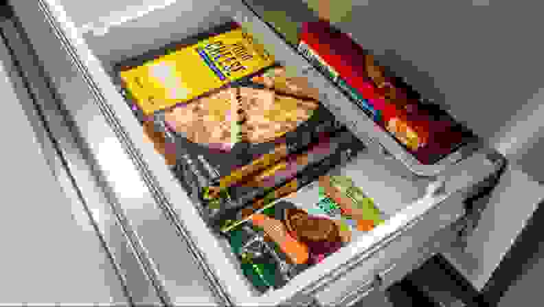 The freezer drawer beneath open, showing off a box of frozen pizza and some frozen burger patties.