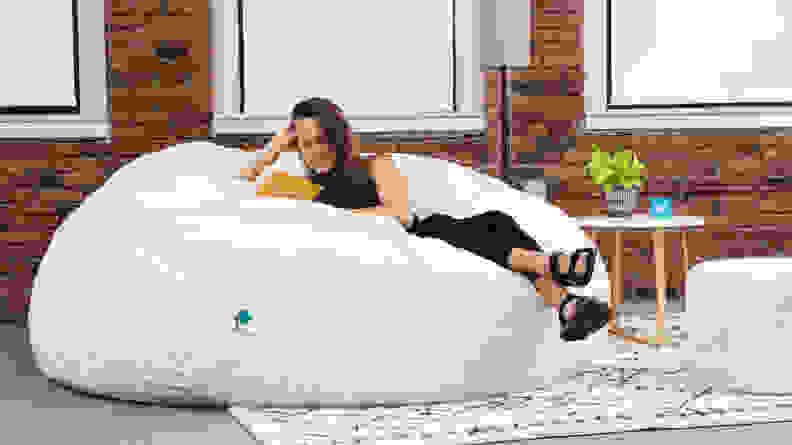 A woman comfortable on a Lovesac bean bag while she reads a book.