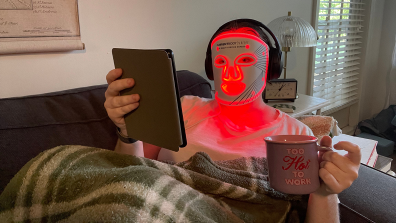 Woman wearing a red light mask and drinking coffee.