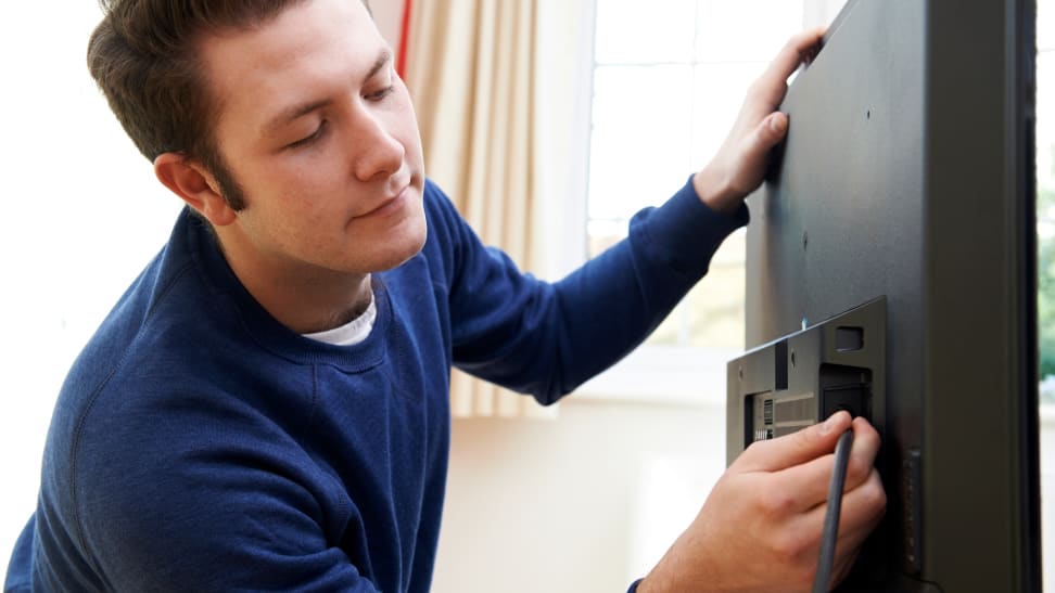 A person plugging a cable into the back of a TV