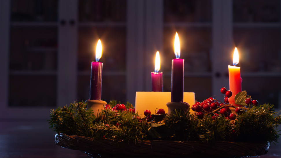 Lit advent wreath with four candles on an evergreen wreath and a white pillar candle in the center.