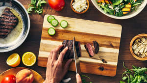 A person slices grilled steak and fresh veggies on a cutting board while preparing colorful HelloFresh meals with salad ingredients.