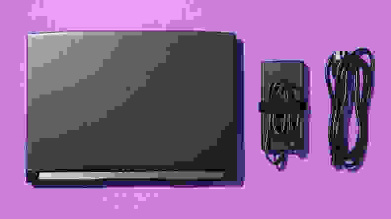 A black laptop and its black charging cables against a purple backdrop.