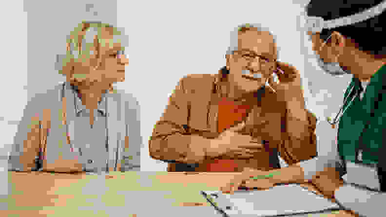 Two elderly patients sit and talk to a nurse about their hearing aid concerns.