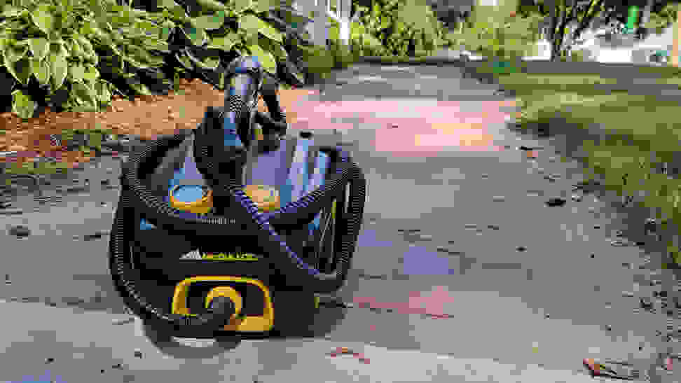 A black and yellow steam cleaner sits on a brick walkway out of doors and next to a green lawn