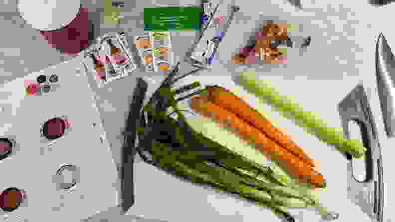 Carrots, shallots and celery on cutting board next to condiment packets and recipe sheet.