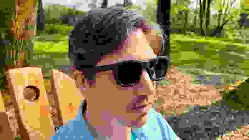 A man wears sunglasses in a blue shirt at a winery while sitting at a wooden chair.