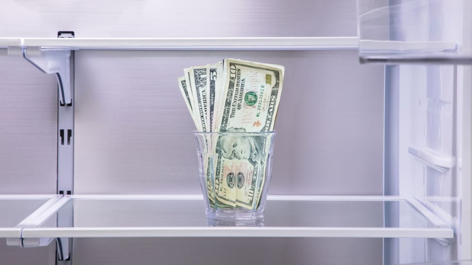 A close-up of the interior of an empty refrigerator with a glass of money on one shelf.