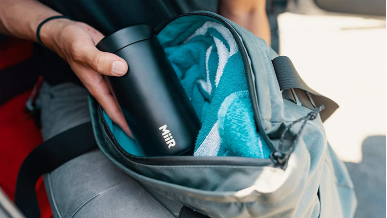 A person is putting a MiiR coffee canister into a backpack.