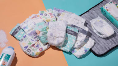 A stack of baby's diapers in the middle a changing mat and baby wipes and a pile of talcum powder.