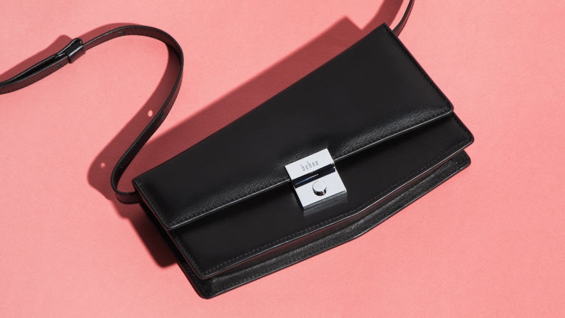 A black handbag lays against a pink surface.