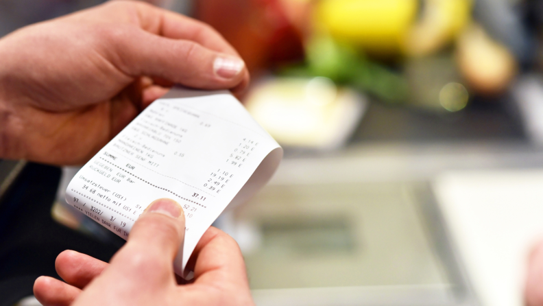 Person reviewing transaction receipt after shopping for food at grocery store.