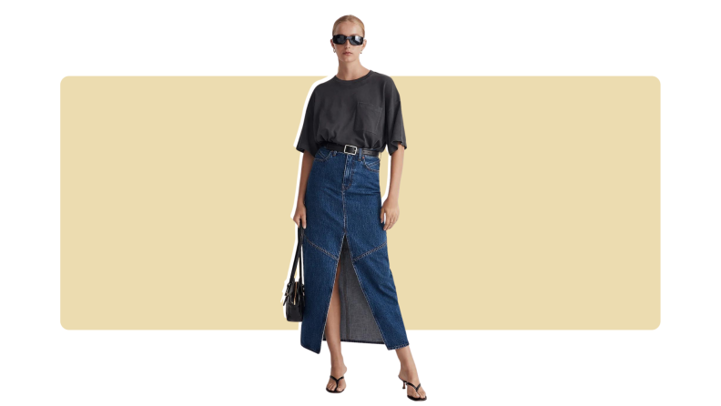 A model wearing a black blouse with a blue denim maxi skirt with a slit in the front.
